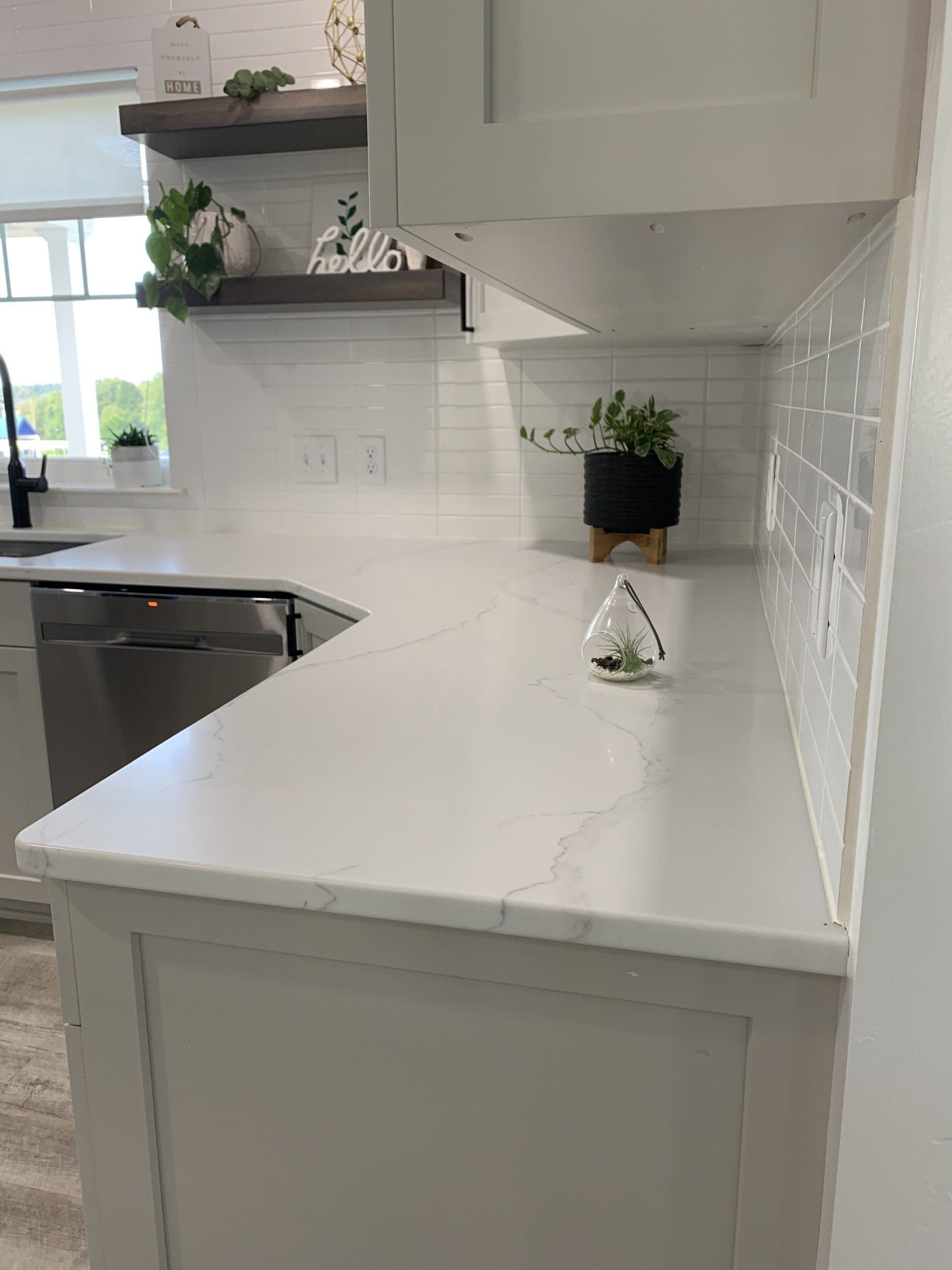 White kitchen countertop with a curved edge, small plant, and white tile backsplash.