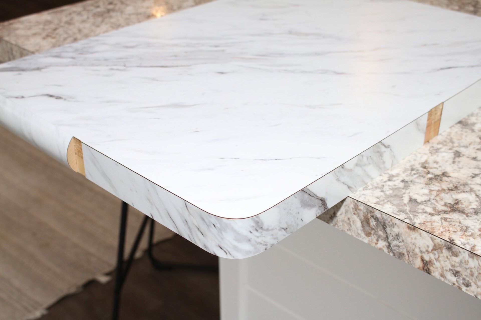 Close-up of a white marble-patterned countertop with a rounded corner, next to a beige speckled surface.