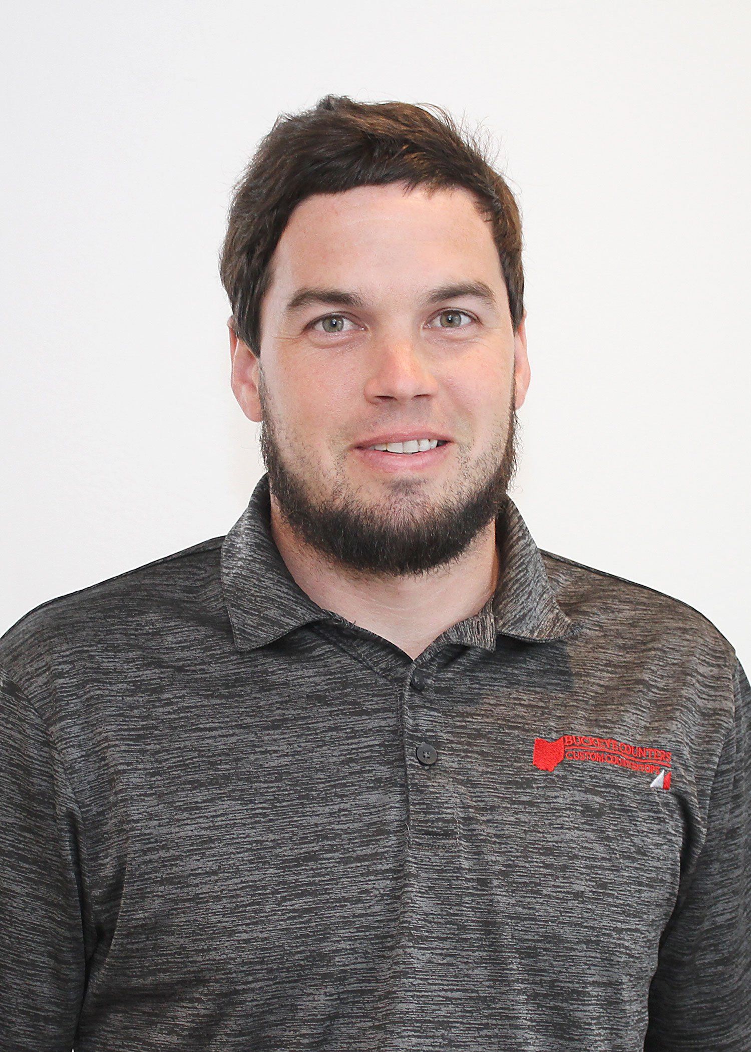 Man in a grey polo shirt smiles, looking at the camera.