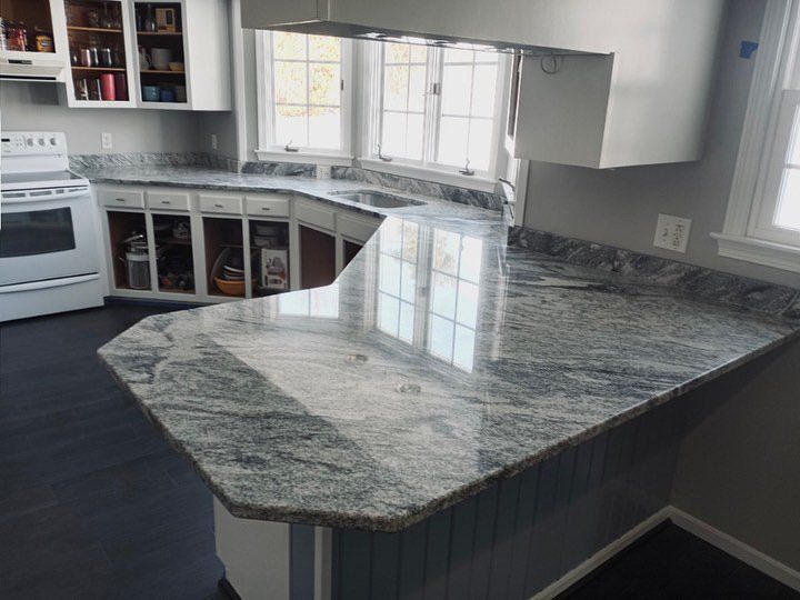 Kitchen with gray and white granite countertop, white cabinets, and dark flooring.