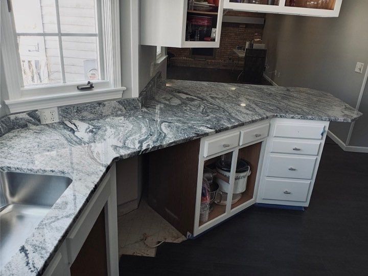 Kitchen with granite countertops and white cabinets near a window.