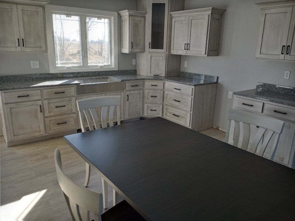 Kitchen with distressed white cabinets, granite countertops, and a dark table.
