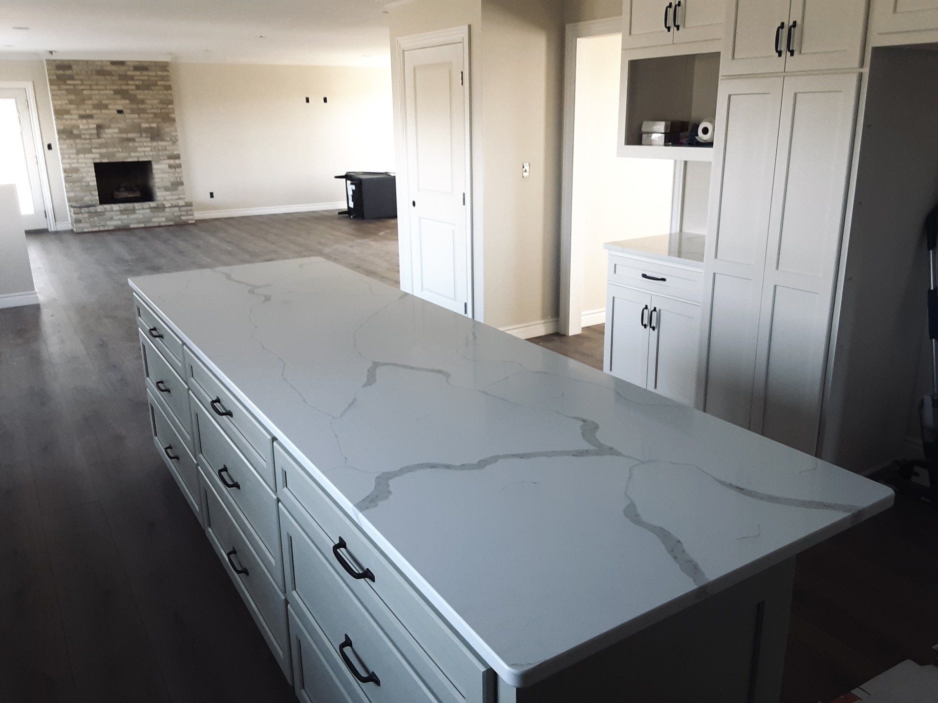 Kitchen remodel with gray island and white cabinets. Fireplace and dark wood floors.