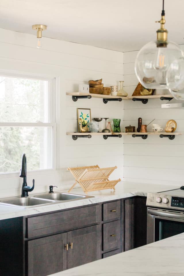 Kitchen with open shelving, dark cabinets, a sink, and a wooden dish rack.