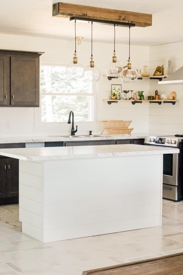 Modern kitchen with white island, dark cabinets, and wood beam light fixture.