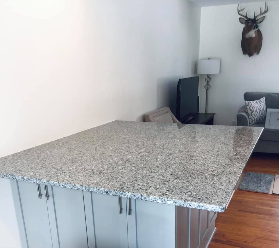 Kitchen island with granite countertop, cabinets, and a living area in the background.