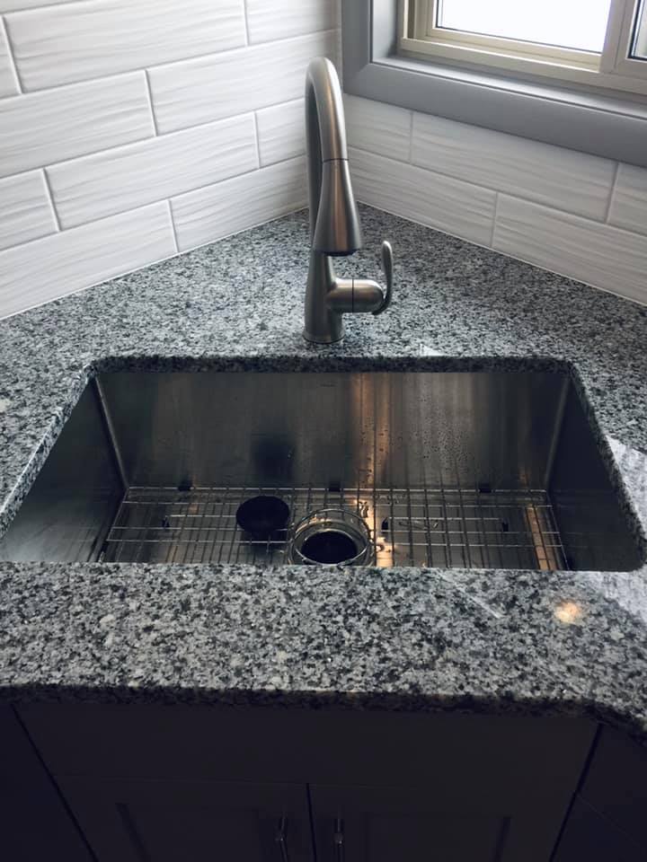 Stainless steel kitchen sink in granite countertop with faucet.