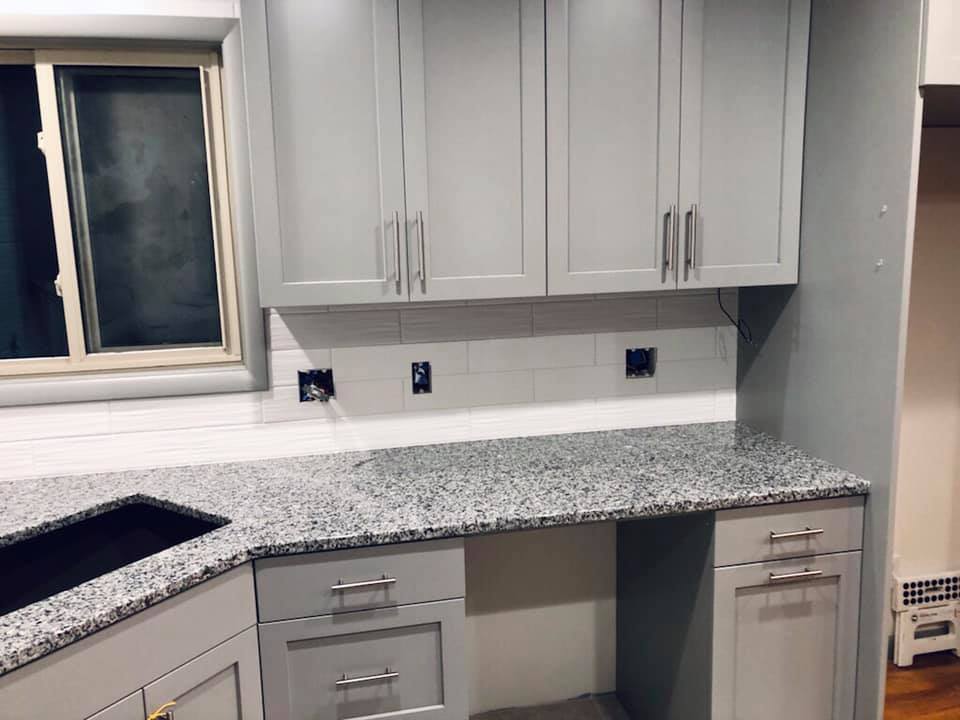 Gray kitchen cabinets and granite countertop with subway tile backsplash.