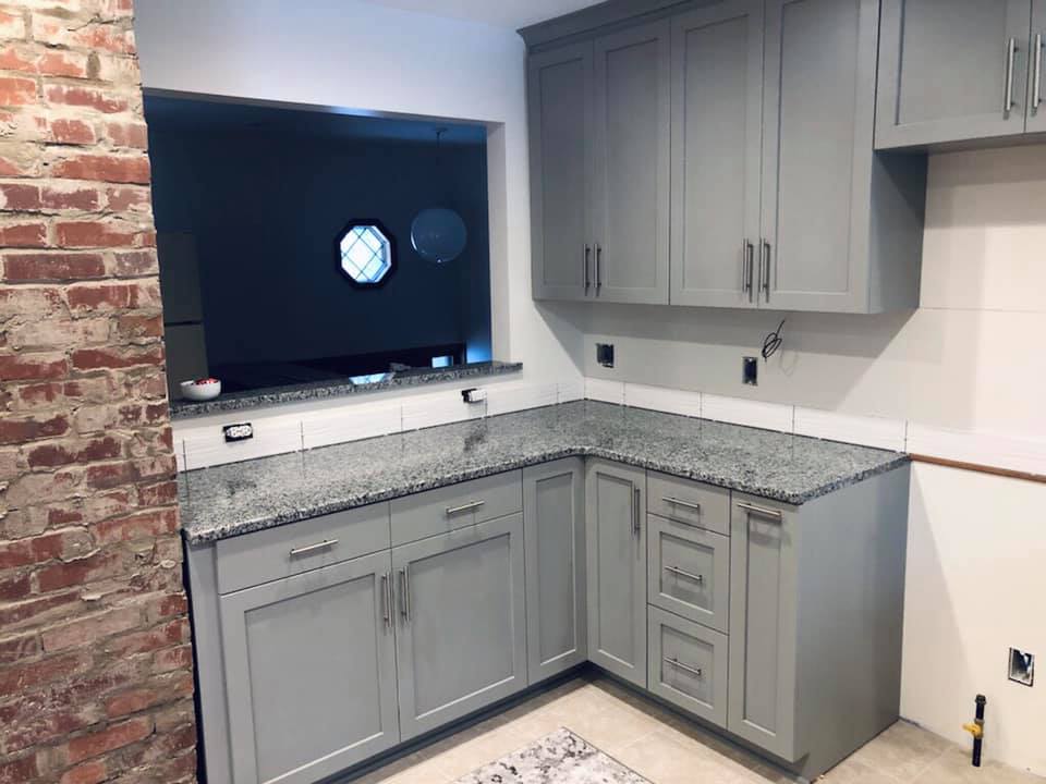 Gray kitchen cabinets with granite countertops, open brick wall, and window.