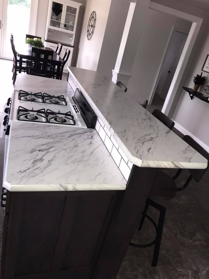 Kitchen island with a marble-patterned countertop and built-in stovetop; dark cabinets, and bar seating.