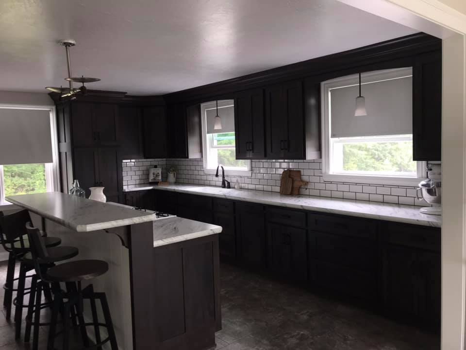 Dark brown kitchen with white countertops, subway tile backsplash, and two windows.