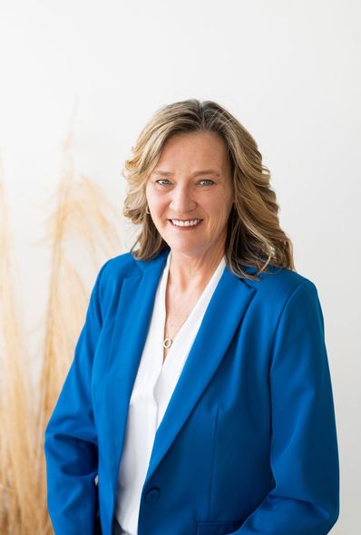 A woman in a blue jacket and white shirt is smiling for the camera.