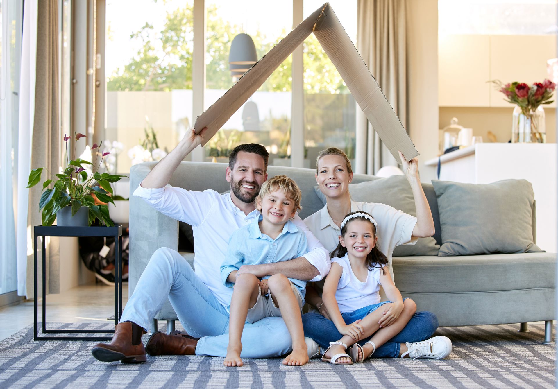 A family is sitting on the floor in a living room holding a cardboard house.