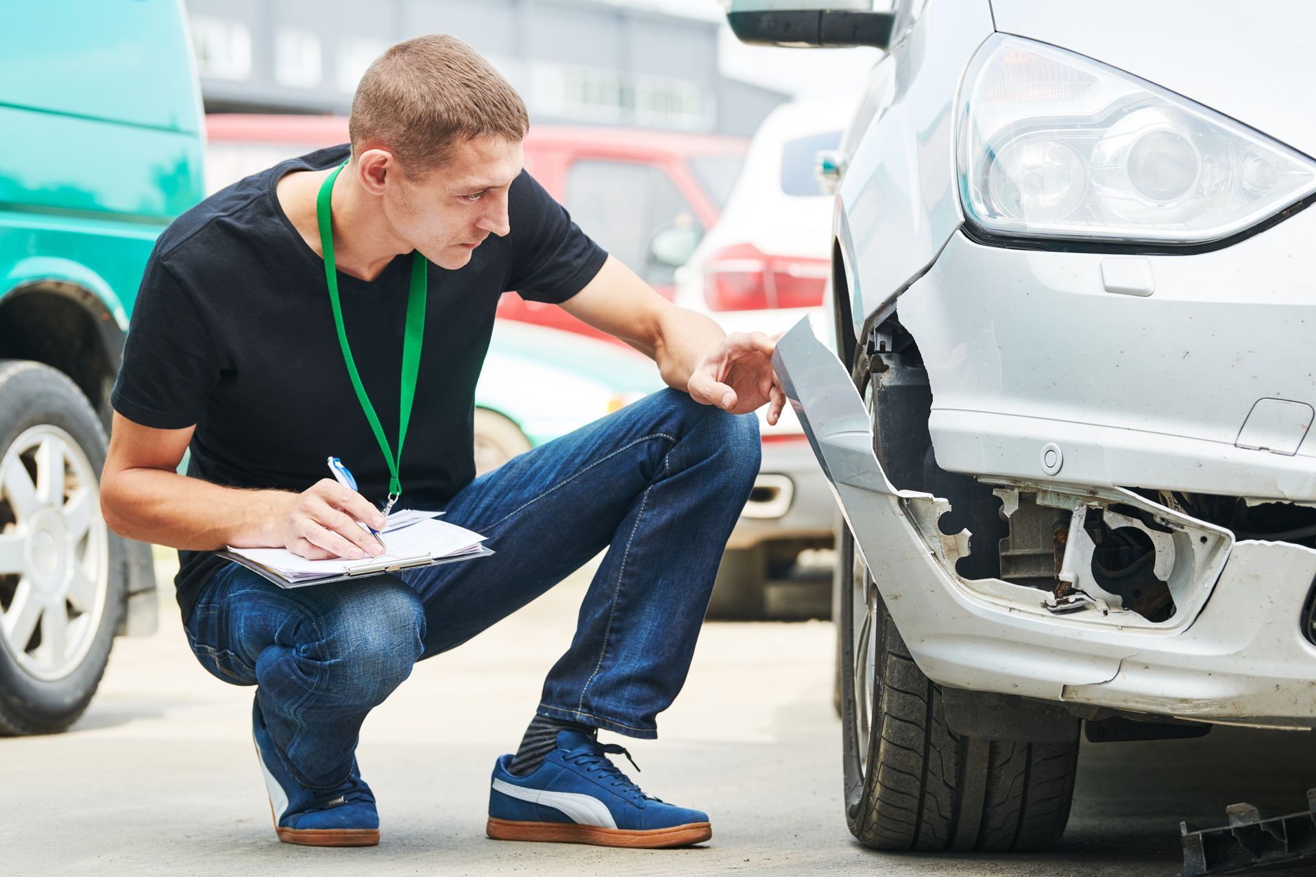 A man is kneeling down in front of a damaged car.