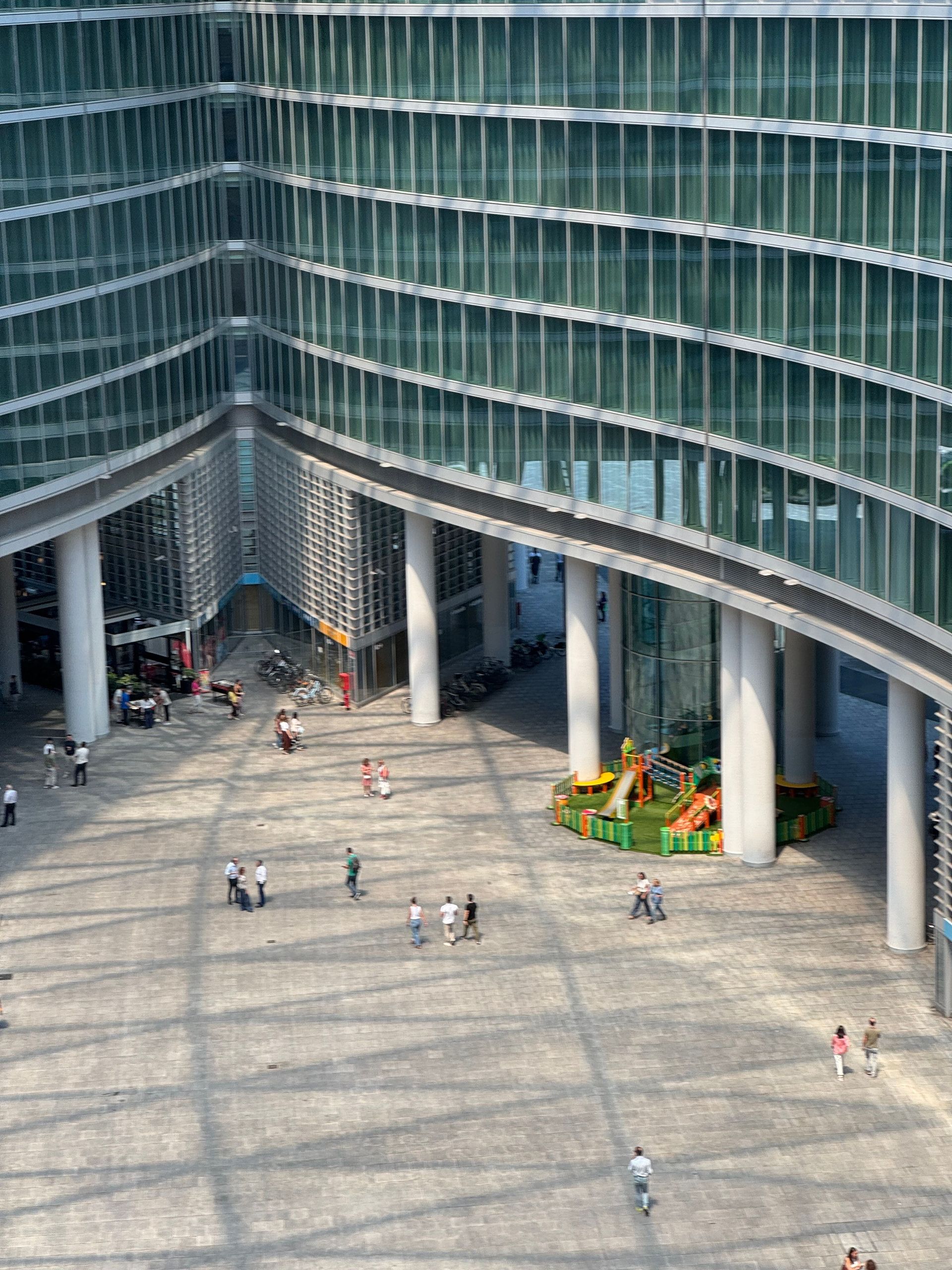 Modern glass-fronted building courtyard with a few people and a small yellow-green playground area