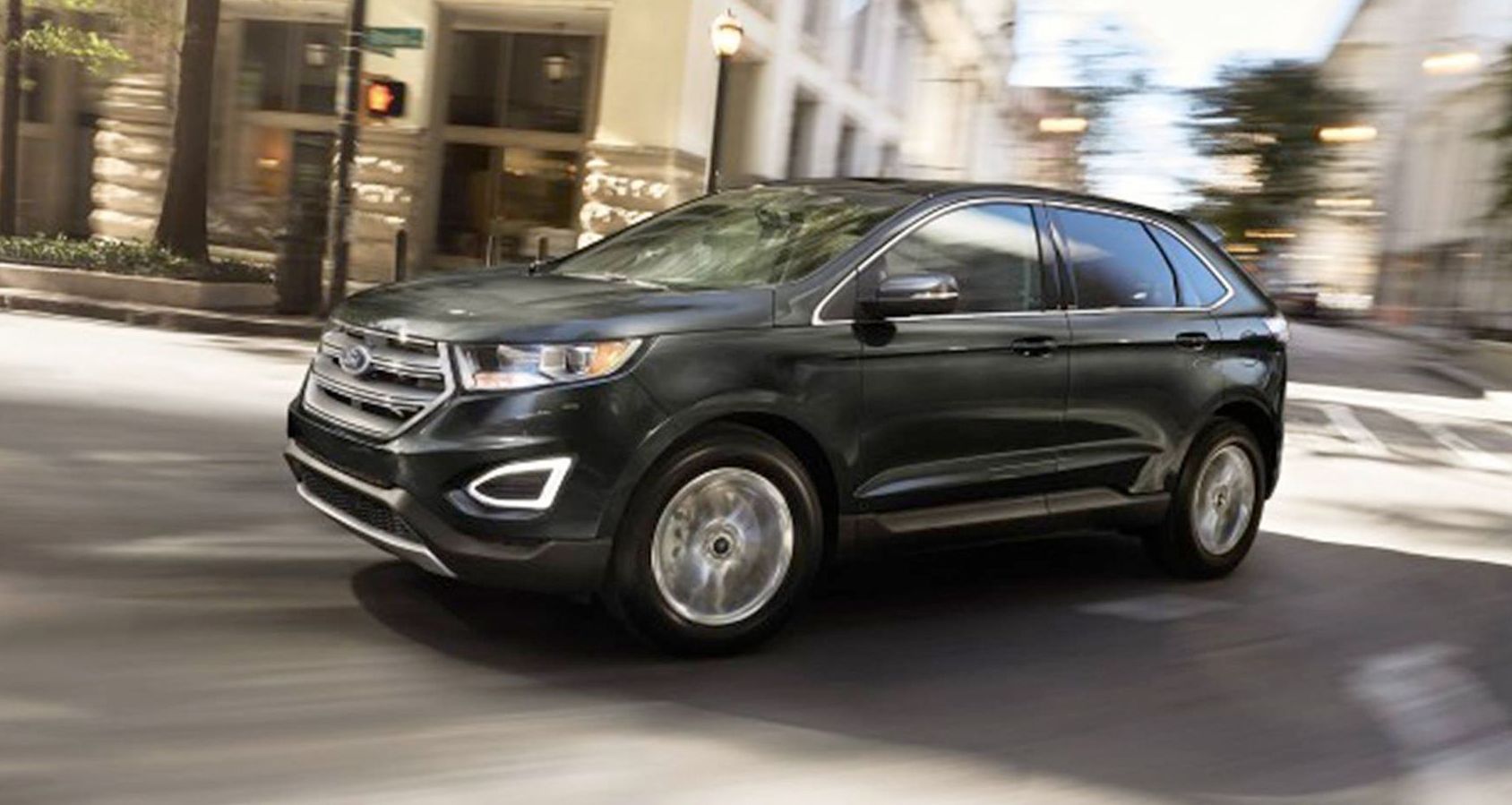A black ford edge is driving down a city street.