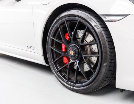 A close up of a white porsche 911 gts with black wheels and red brake calipers.
