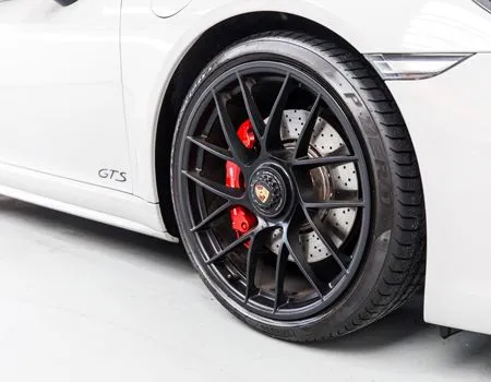A close up of a white porsche 911 gts with black wheels and red brake calipers.