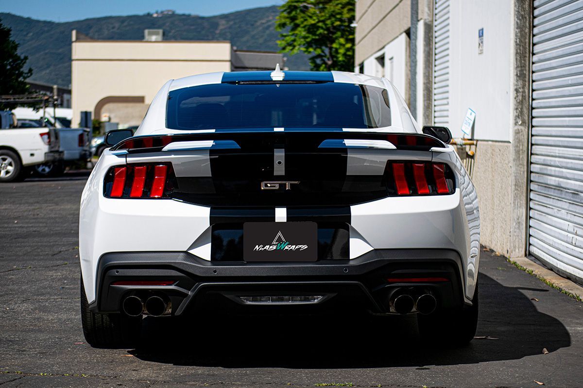 A white ford mustang with black stripes is parked in front of a building.