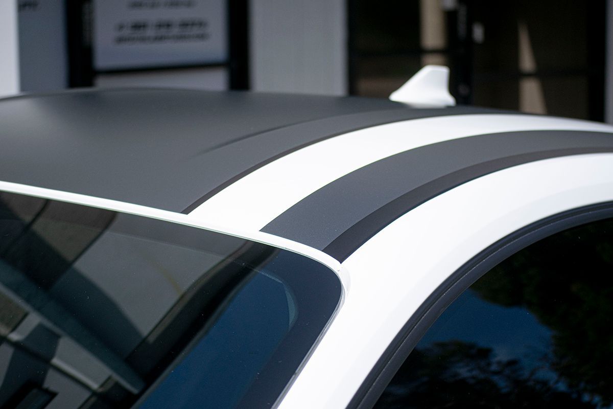 A white mustang with black stripes is parked in front of a building.