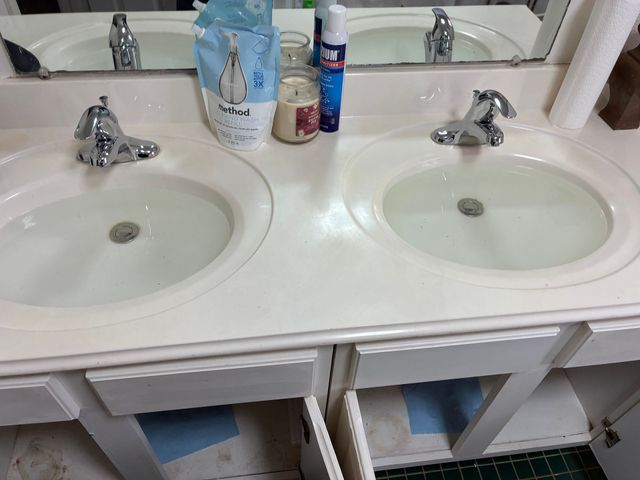 Two white bathroom sinks with chrome faucets and toiletries on the counter, with mirrors above them.