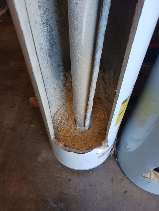 Close-up of a rusted, dirt-filled metal pipe or column base on a concrete floor.