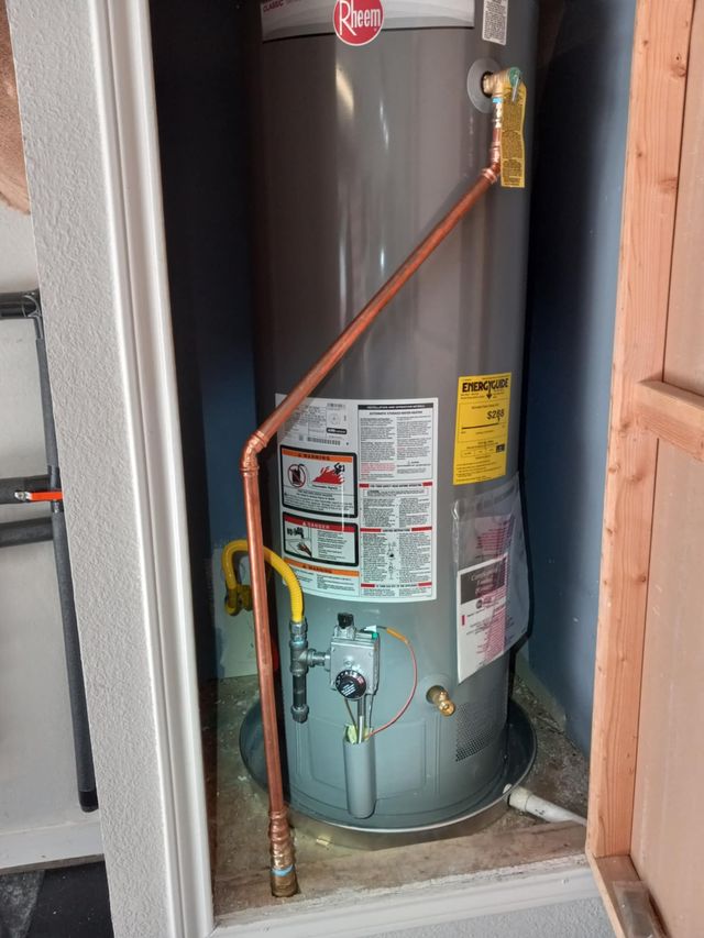 Tall gray water heater with copper piping in a narrow utility closet, viewed through an open doorway