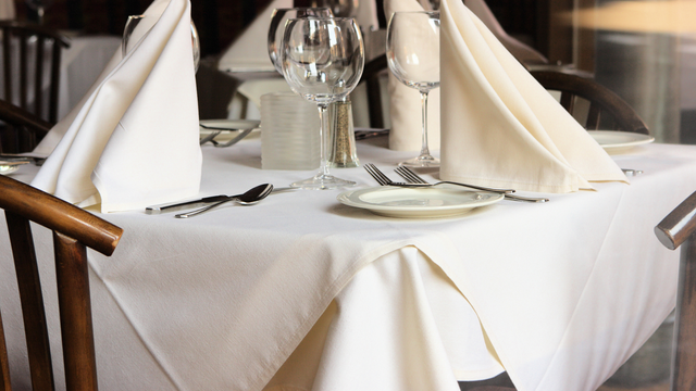 Neatly set restaurant table with white tablecloth, folded napkins, plates, glasses, and cutlery