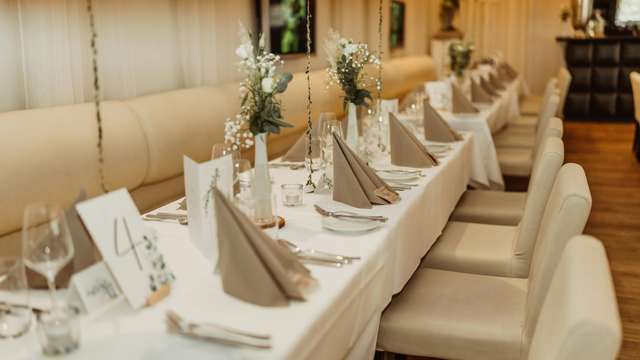 Elegantly set banquet table with white linens, folded napkins, floral centerpieces, and cream chairs in a warm dining room