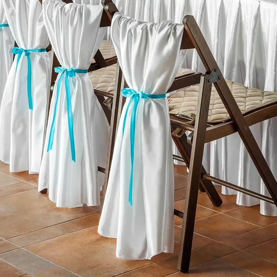 White chairs with turquoise sashes lined up on a tiled patio under a wooden table