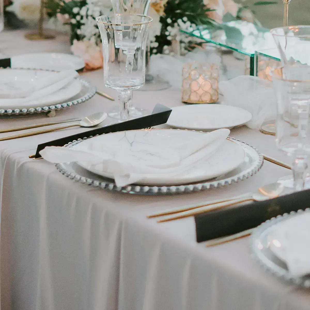 Elegant white table setting with gold utensils, folded napkins, and glassware for a formal event