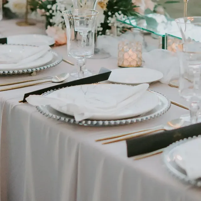 Elegant wedding reception table with white plates, gold cutlery, crystal glasses, and floral decor