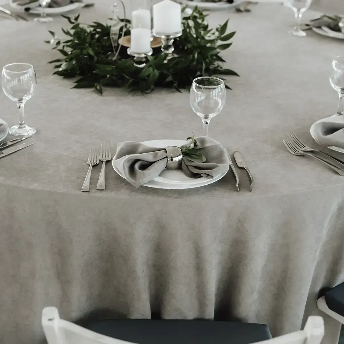Elegant dining table with gray linens, place settings, and a greenery candle centerpiece