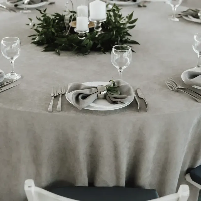 Elegant table setting with gray linens, white plates, glassware, and a greenery centerpiece with candles