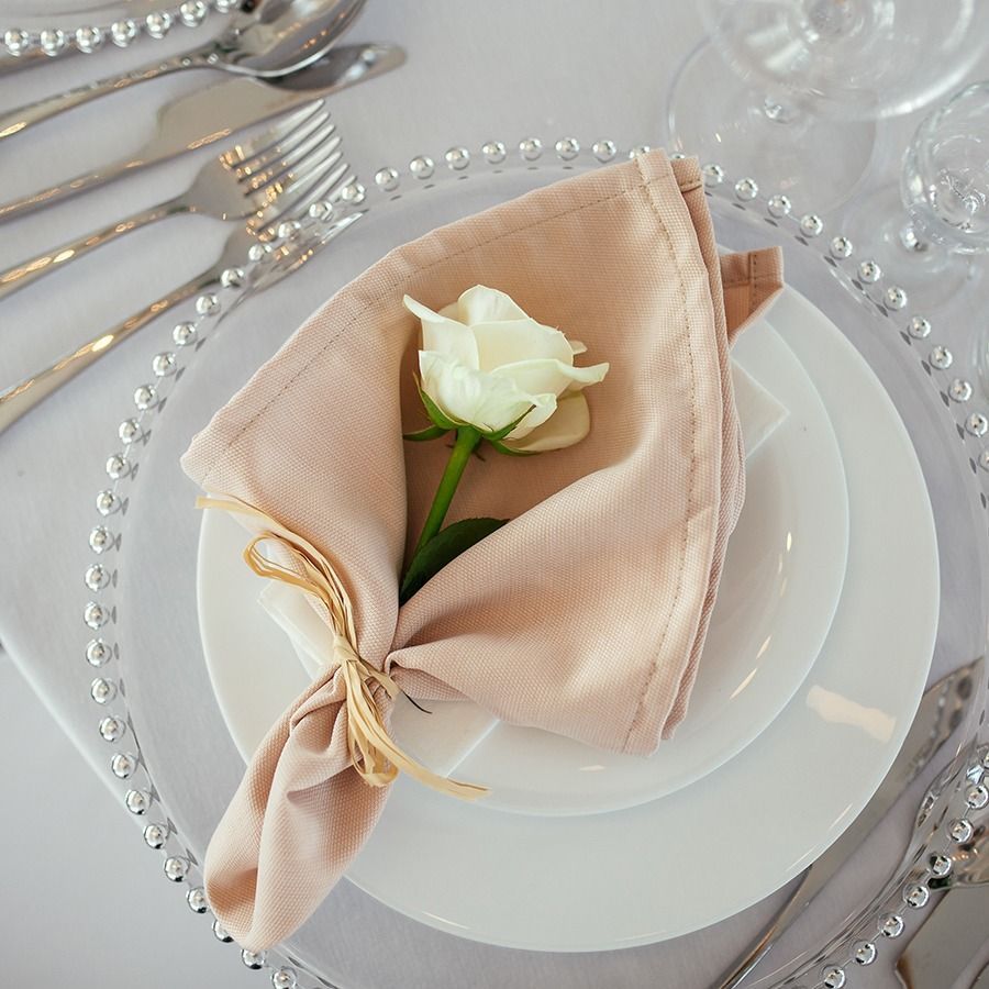 Elegant table setting with a blush napkin, white rose, and pearl-trimmed charger plate