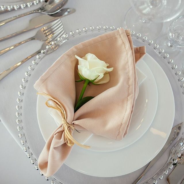 Elegant table setting with a beige napkin holding a white rose on a white plate