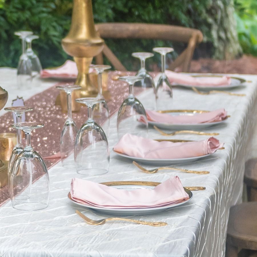 Elegant outdoor table setting with pink napkins, upside-down glasses, and gold candleholders on a white tablecloth