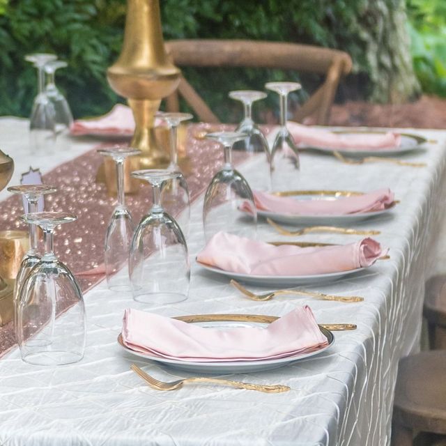 Elegant outdoor dining table set with pink napkins, gold accents, and upside-down wine glasses