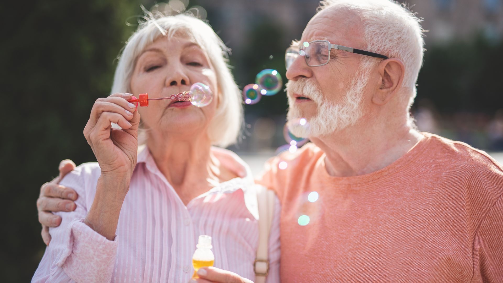 An elderly couple is blowing soap bubbles together.