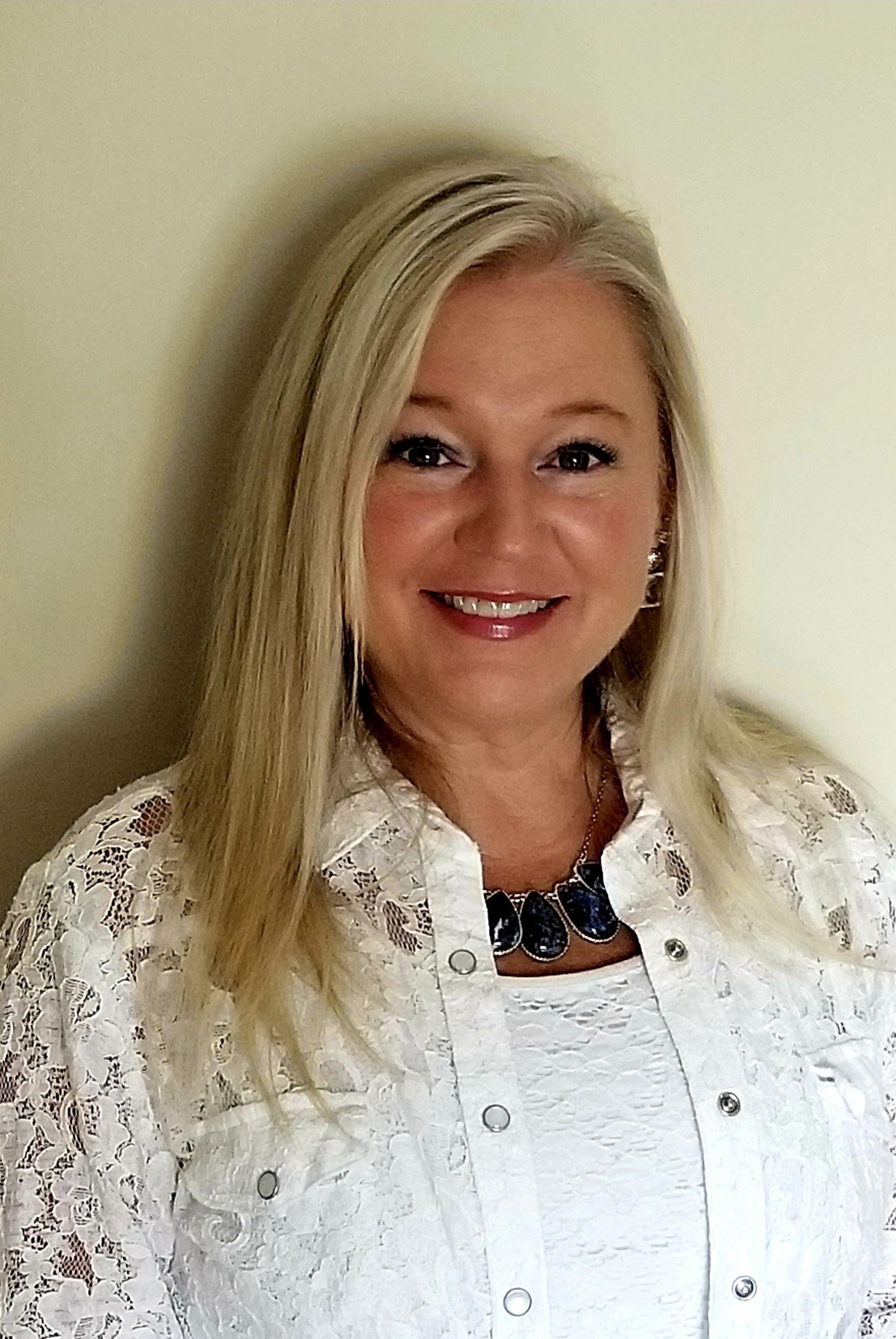 A woman in a white shirt and necklace is smiling for the camera.