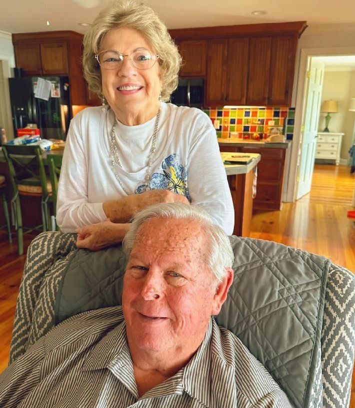A woman is standing next to a man in a chair