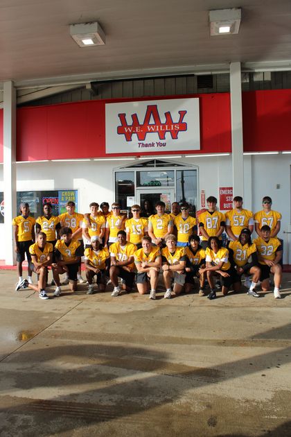 A group of young men are posing for a picture in front of a gas station.