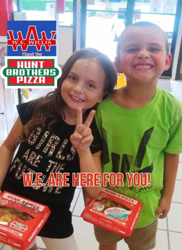 A boy and a girl are posing for a picture in front of a sign that says hunt brothers pizza