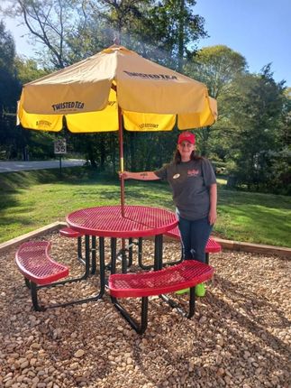 A woman is standing next to a red picnic table under a yellow umbrella.