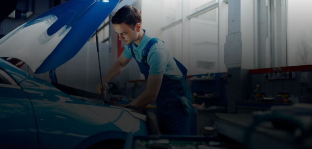 Mechanic working under open car hood in a bright auto repair shop