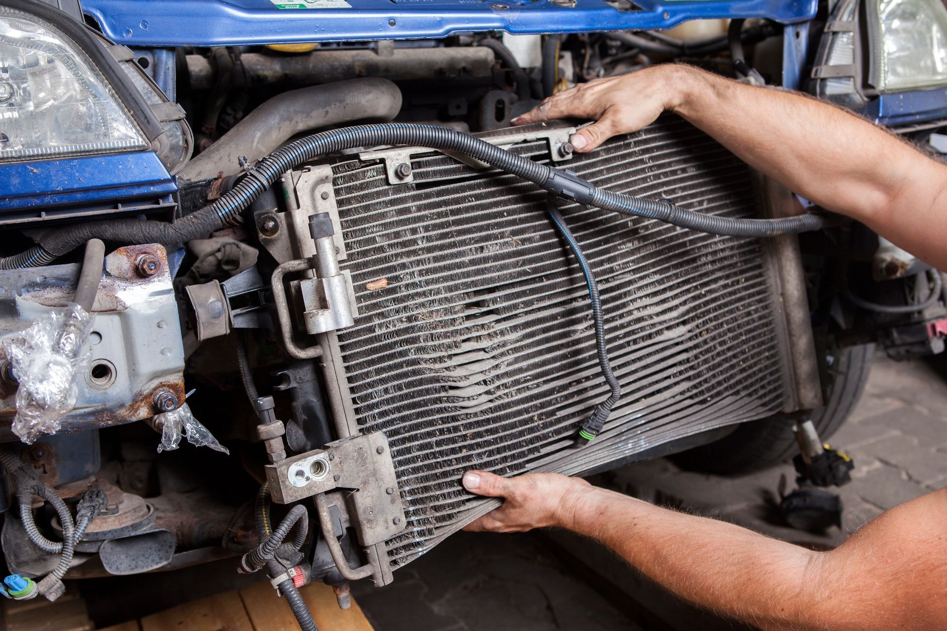 Mechanic removing a damaged car radiator from the front of a blue vehicle