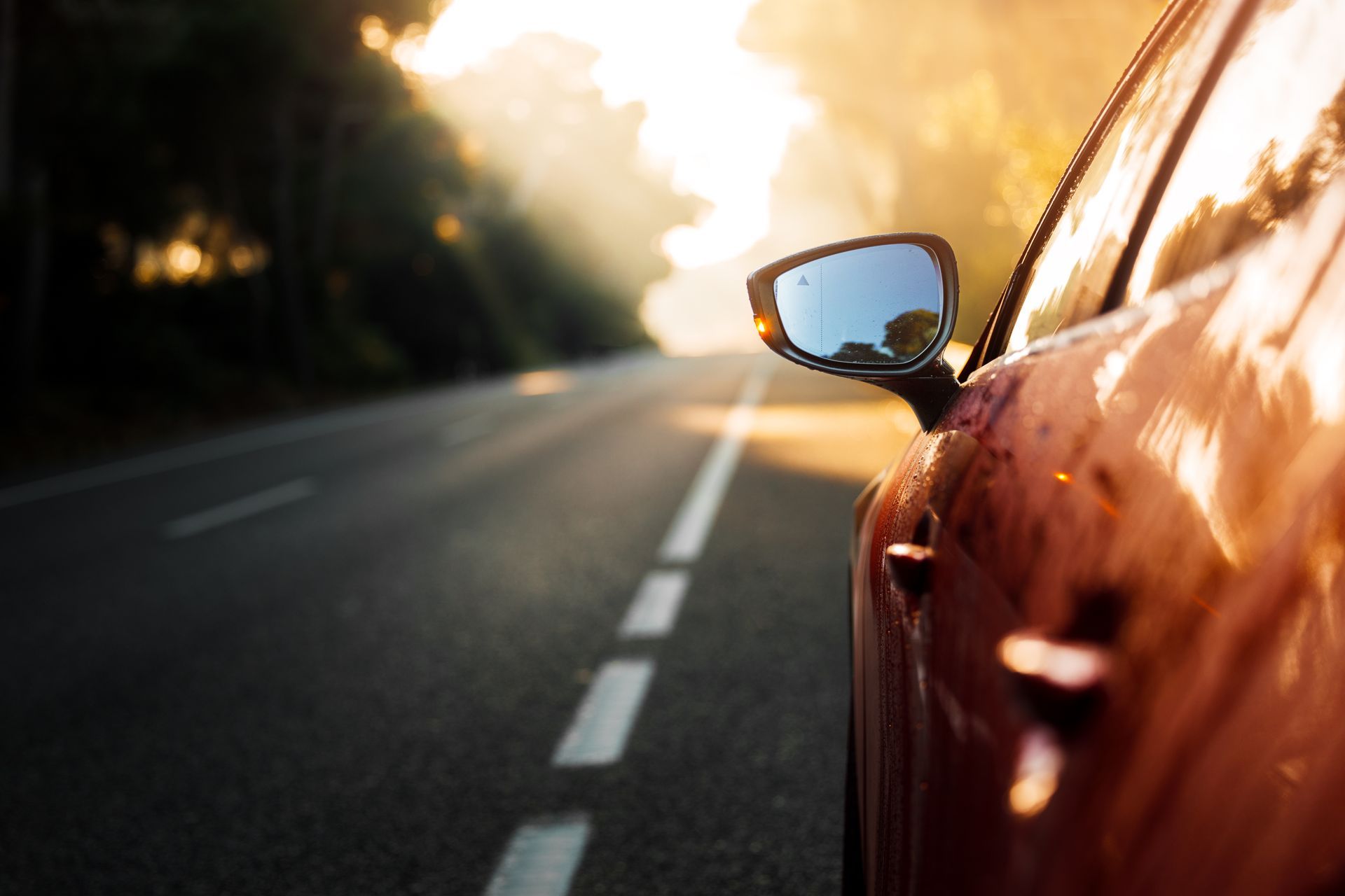 Car driving on an empty road at sunset, with warm sunlight reflecting on the orange body.