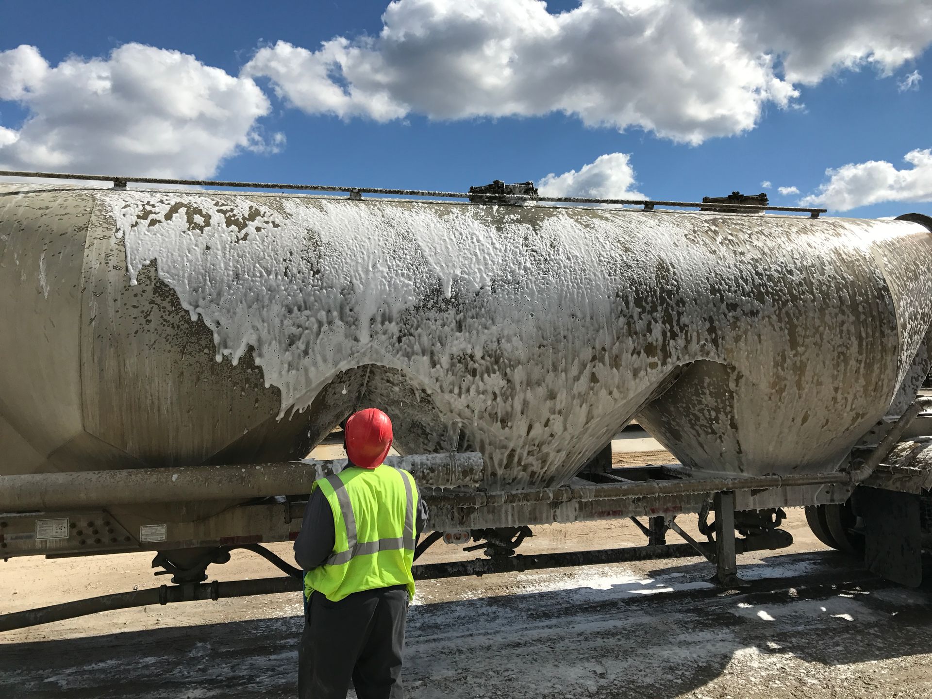 Worker in safety vest inspects a cement tanker covered in white material under a cloudy sky.