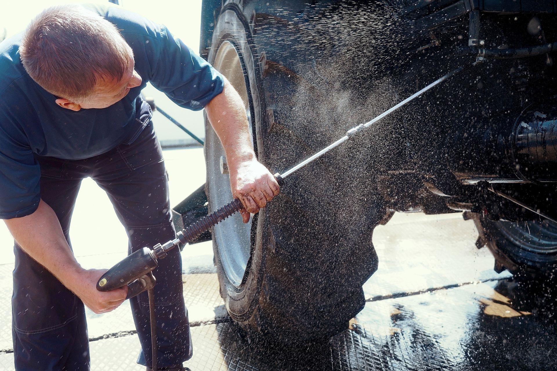 Man washing a large tractor tire with a pressure washer.