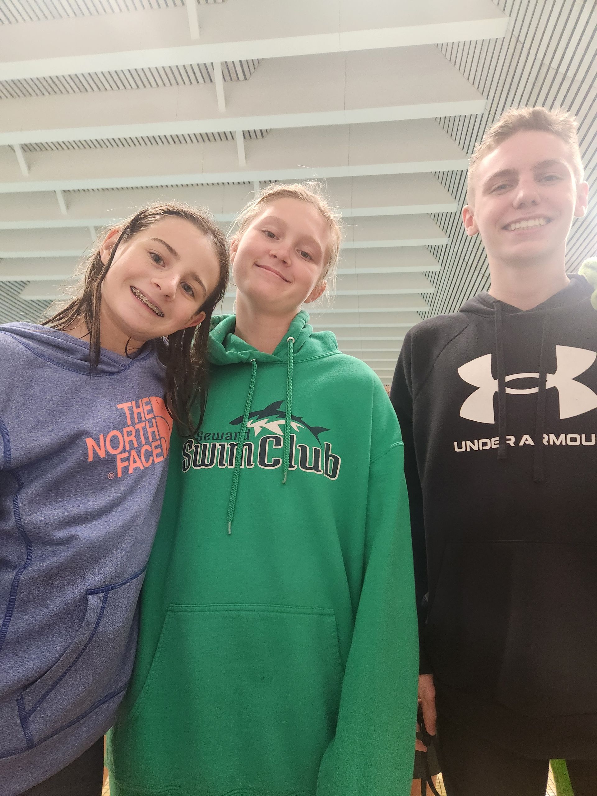 Three smiling people in hoodies, indoors under a white ceiling.